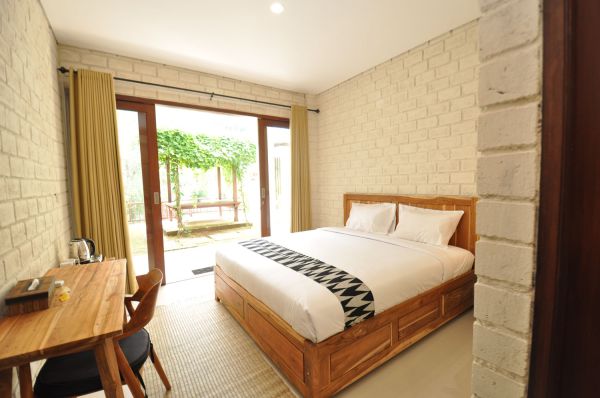 Cozy tropical bedroom with wooden bed, white brick walls, desk, and sliding doors to vine-covered garden.